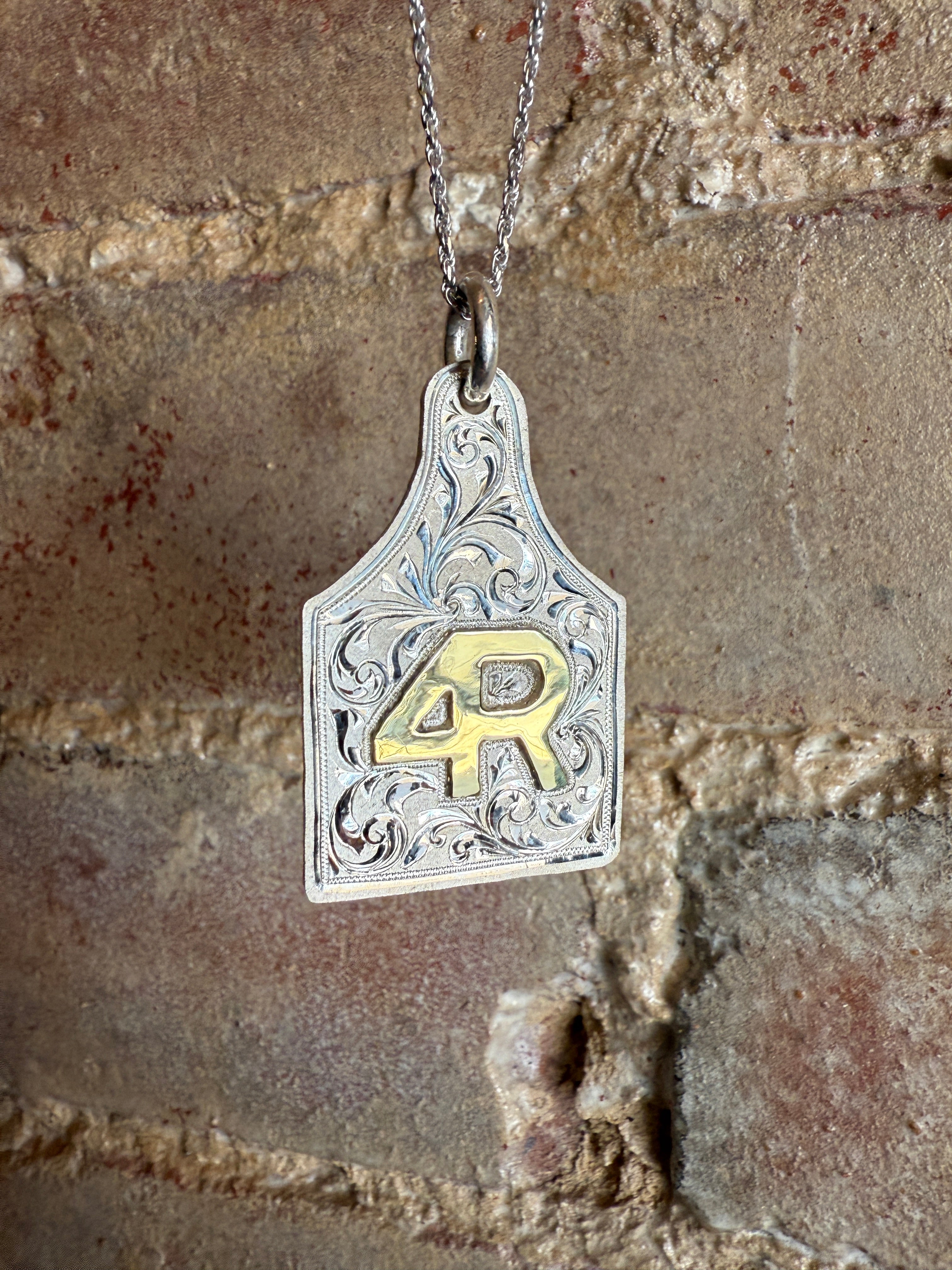 Decorative silver and brass pendant on a chain against a stone wall background
