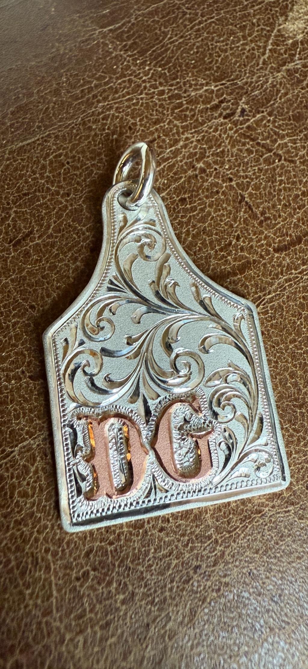 Decorative silver and copper pendant with 'DG' on a brown leather background