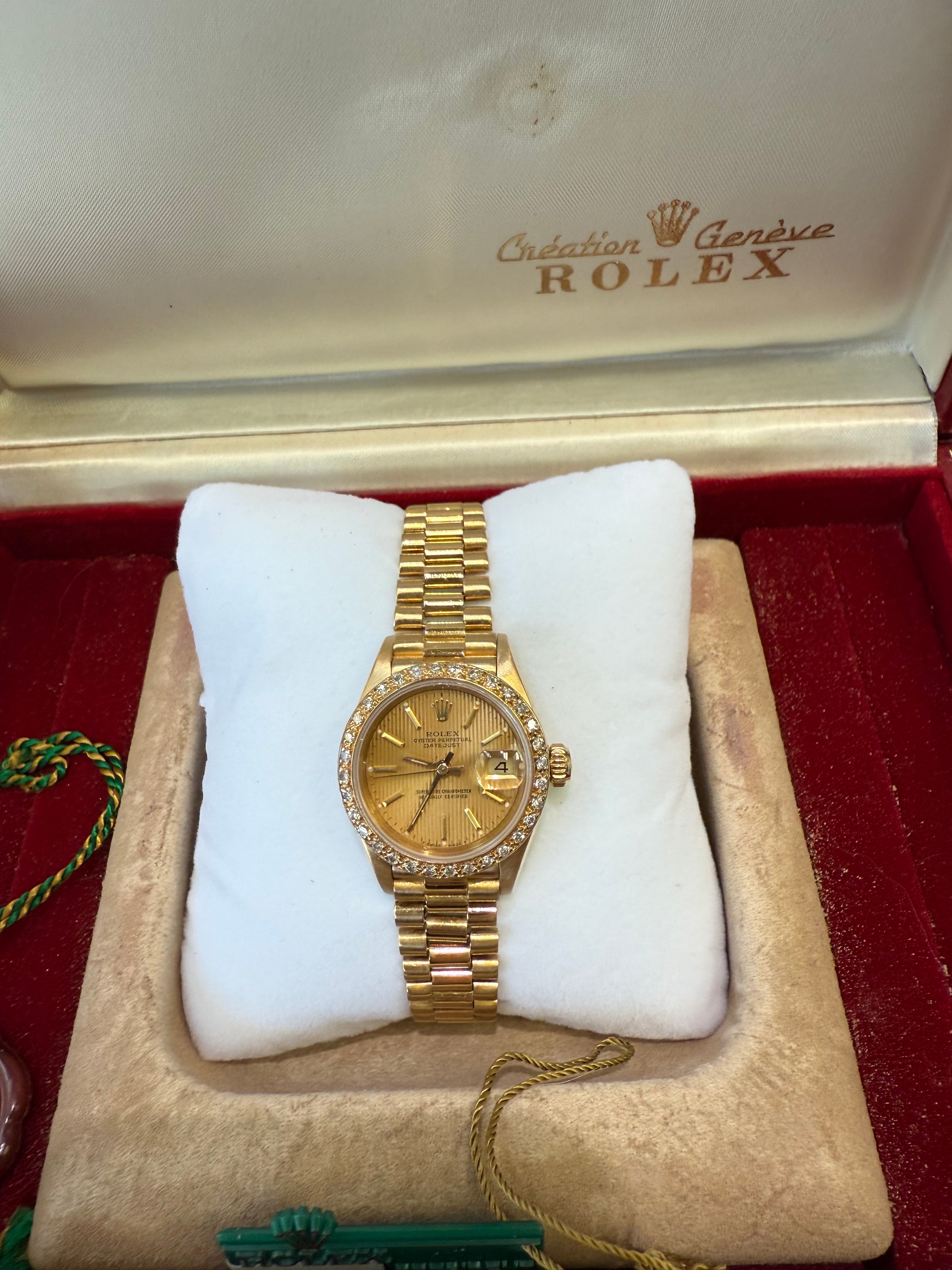 Gold watch on a white cushion with a Rolex box in the background
