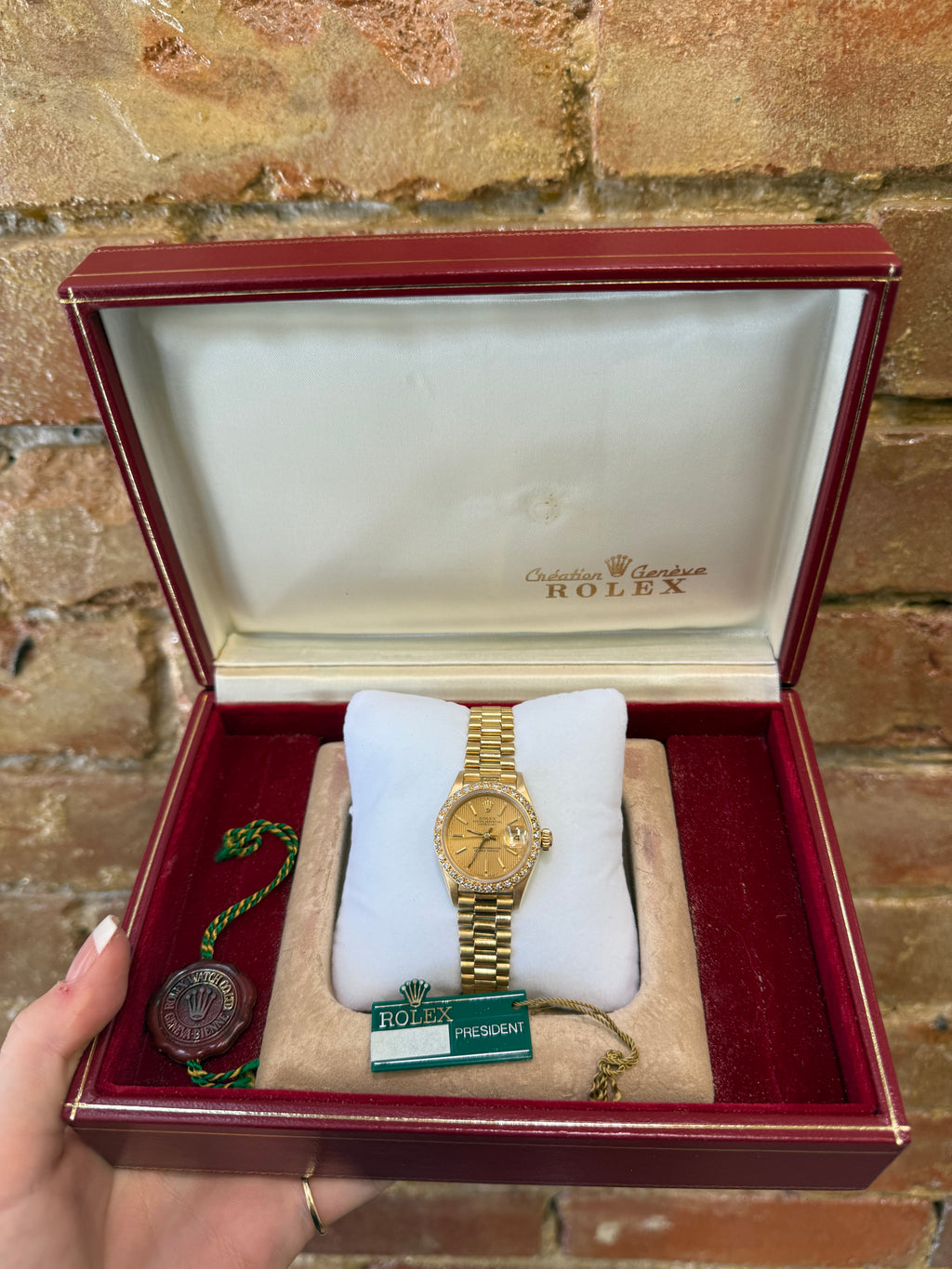 Gold watch in a red Rolex box against a stone wall background