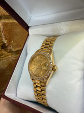 Load image into Gallery viewer, Gold wristwatch with diamond-studded bezel on a white cushion inside a jewelry box.
