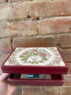Decorative jewelry box with floral patterns held against a brick wall.