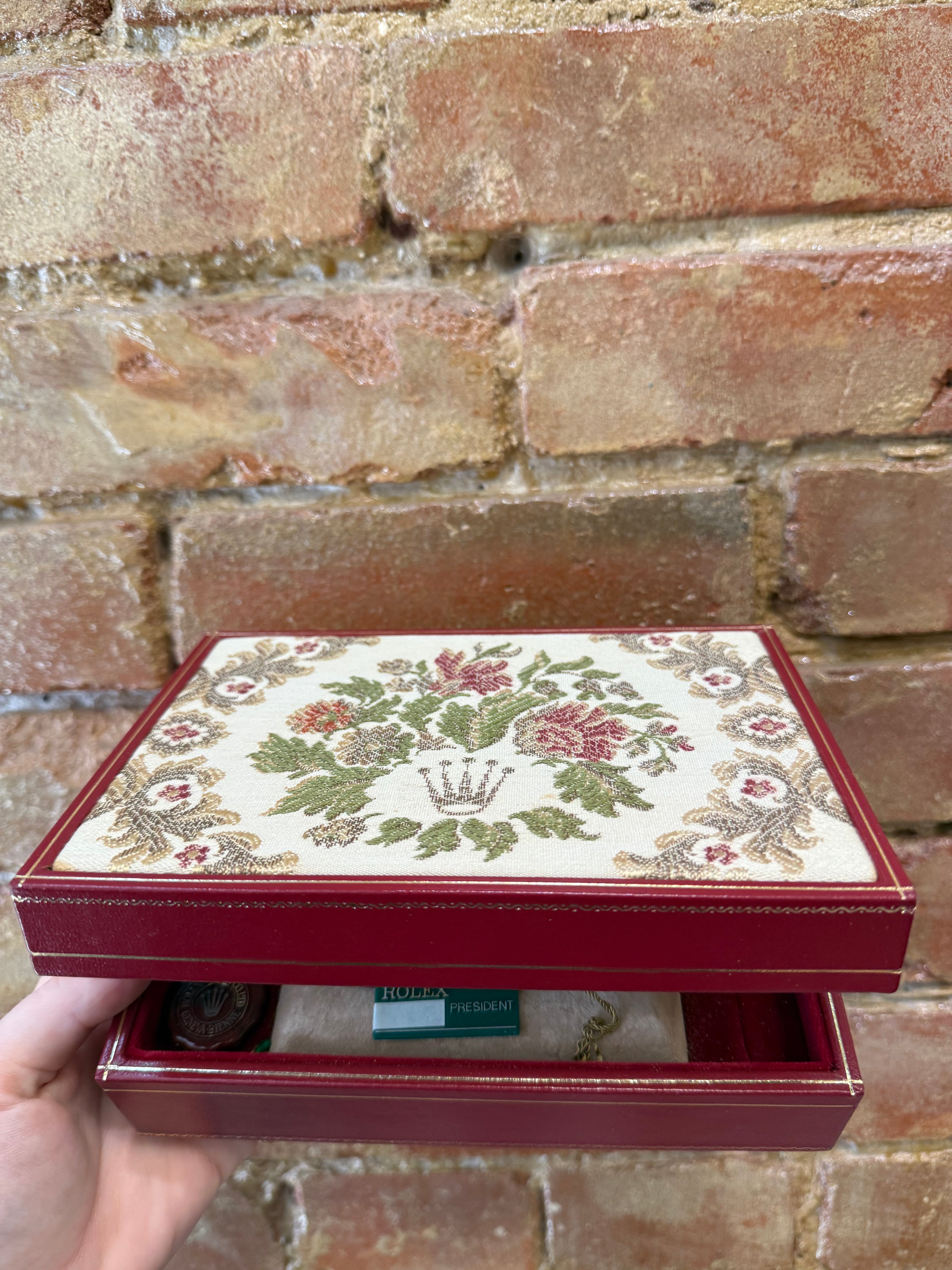 Decorative jewelry box with floral patterns held against a brick wall.