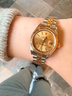 Gold and silver watch on a wrist with a neutral background