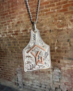 Silver pendant with engraved design and 'YW' initials against a brick wall background